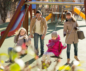 family with two girls having fun on swings outdoors