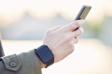 Men's hand wearing a smart watch and holding mobile phone