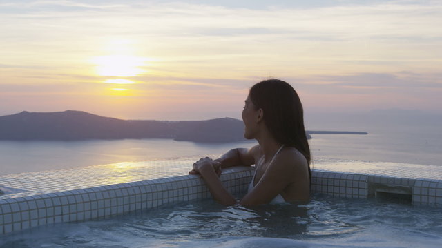 Vacation woman enjoying sunset in Spa on Travel. Happy woman in white bikini getting out of swimming pool. Sexy woman sitting at the edge of swimming pool enjoying her vacations on Santorini, Greece.
