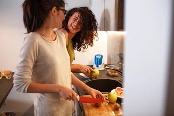 Photo sur Plexiglas Cuisinier Jeunes amies en cuisine préparant ensemble un repas végétarien.Préparer une salade de fruits.Soir.