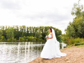 Fototapeta na wymiar bride in a white dress with wedding bouquet at the lake