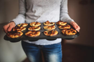Young woman holding a tray with muffins at the kitchen