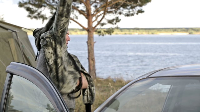 hunter or fisherman puts a special camouflage clothing. In the evening, at sunset, near the car, the tree and the river