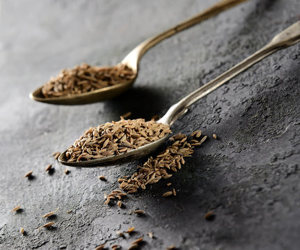cumin seeds in metal spoon on a dark background