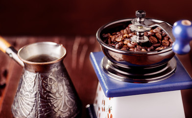 Mechanical coffee grinder, old copper cezve and coffee beans. Over wooden table as background.