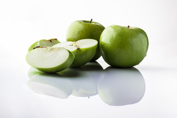Two whole green apples and one sliced on white background directly from side with reflection