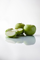 Two whole green apples and one sliced on white background directly from side with reflection vertical