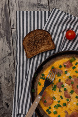 Close up shot of omelette with ham in old rustic plate and chopped spring onion. Photographed from above on old wooden rustic table.