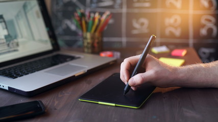 Creative businessman writing on graphic tablet while using laptop in office