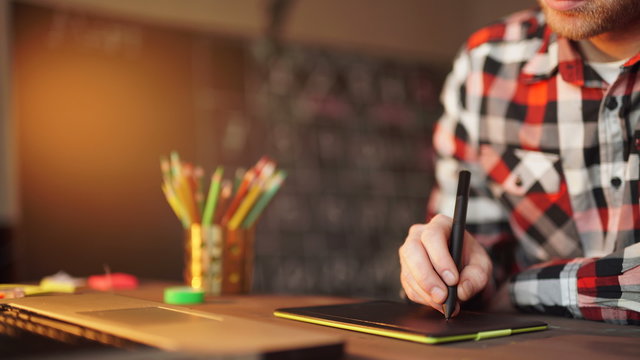 Creative businessman writing on graphic tablet while using laptop in office