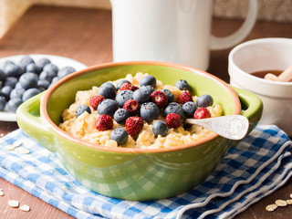 Closeup of oatmeal porridge with blueberries and wild strawberries on a kitchen napkin on wooden table
