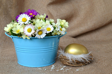 Golden Easter egg in the nest and spring flowers