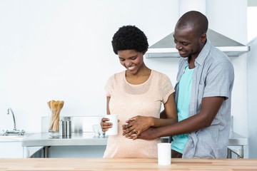 Pregnant couple embracing while having cup of coffee