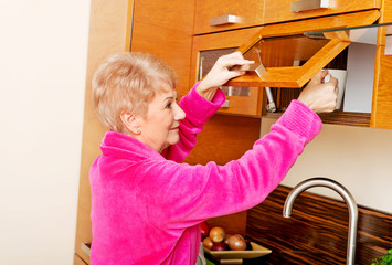 Smile senior woman taking mug from a kitchen cabinet
