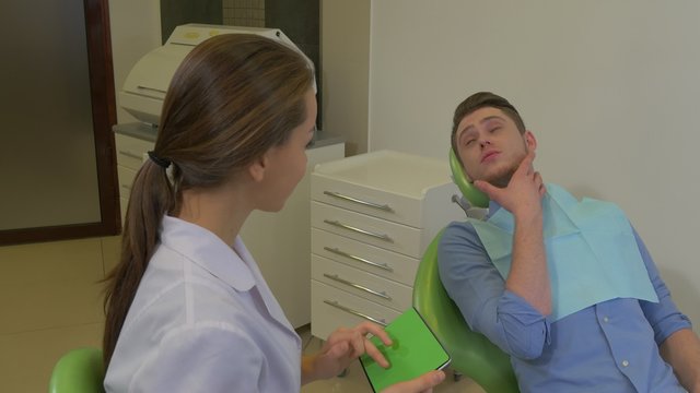 Patient Touches His Jaw Dentist Clicks Tablet Listening to a Patient Client is Talking Complaints Room of Dental Clinic Young Female Doctor Male Client
