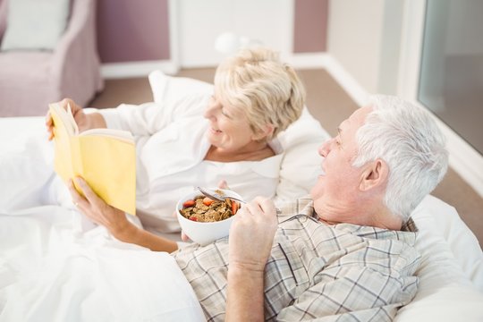 Couple reading book while having breakfast on bed