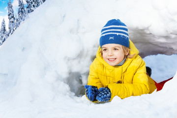 Fototapeta na wymiar Little boy in yellow crawl through snow tunnel