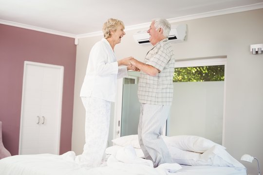 Cheerful Senior Couple Jumping On Bed