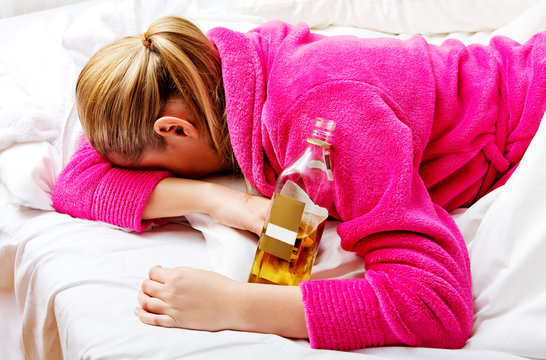 Young worried woman drinking alcohol in bed