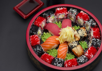 Sushi set with ginger and wasabi on a wooden round plate over black background