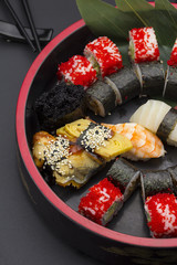 Sushi set with ginger and wasabi on a wooden round plate over black background