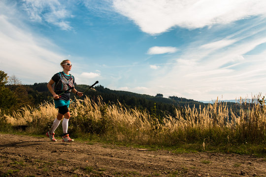 female ultra trail runner with poles training in the mountains with blue sky