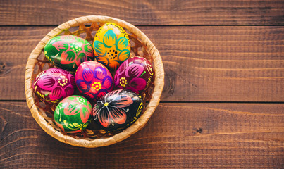 Beautiful painted colorful Easter eggs in a wickerwork basket on old brown wooden background