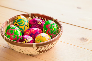Beautiful painted colorful Easter eggs in a wickerwork nest on a light wooden background