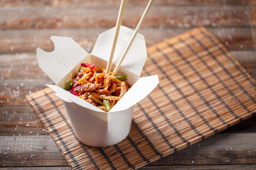Noodles with pork and vegetables in take-out box on wooden table