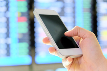hand holding smartphone on a flight information board in the airport background