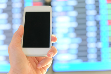 hand holding smartphone on a flight information board in the airport background