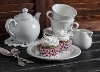 Chocolate cupcakes with coconut cream and a tea set on wooden background