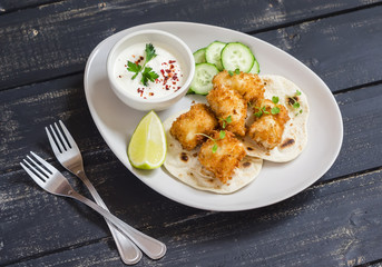 Crispy fried fish on a homemade tortilla on a dark wooden background