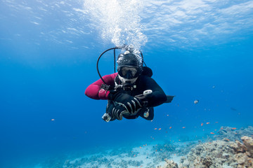 Scuba-duiker drijvend over koraalrif in de rode zee en kijkend naar de camera.