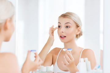 young woman putting on contact lenses at bathroom