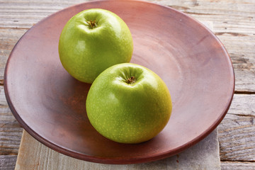Two green apples on rustic ceramic plate