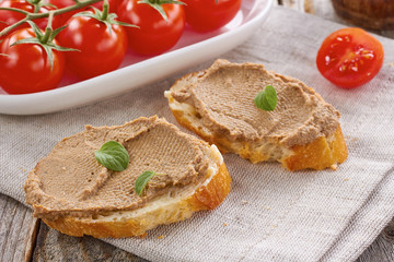 Homemade chicken liver pate on  baquette and tomatoes on textile napkin