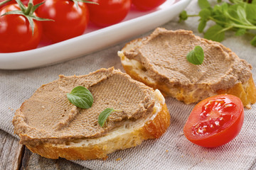 Homemade chicken liver pate on  baquette and tomatoes on textile napkin