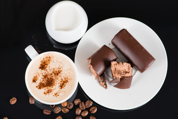 a cup of cappuccino and chocolate glazed curd cake on a black ba