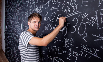 Student writing on big blackboard with mathematical symbols