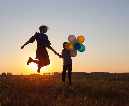 happy mother and son jumping with balloons outdoor