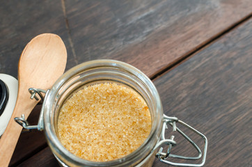 brown sugar with wooden spoon in bottle on wood table, selective focus.