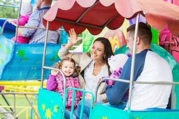Obraz na płótnie Canvas Father, mother, daughters enjoying fun fair ride, amusement park