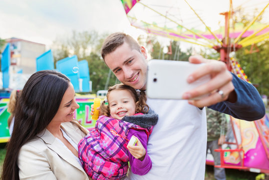 Father, mother and daughter in amusement park taking selfie