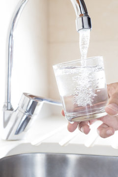 Filling glass of water in hand from kitchen faucet. Concept of safe water and healthy life