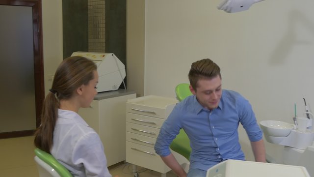 Client Comes Dentist Invites Him to Sit Down Man is Smiling Talking Woman is Wearing a Gloves Going to Examine Dental Clinic Female Doctor Male Client