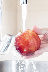 Close up male hands washing apple under water in sink. Washing organic fruit. Concept of healthy and hygiene habits.
