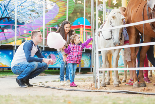 Family with daughter stroking pony in amusement park