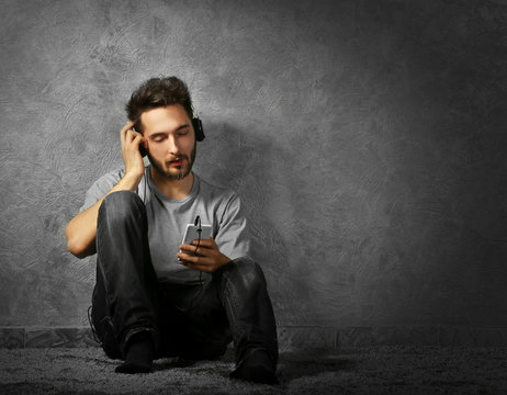 Young bearded man listening music with headphones on grey wall background