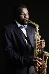 African American jazz musician playing the saxophone on grey background